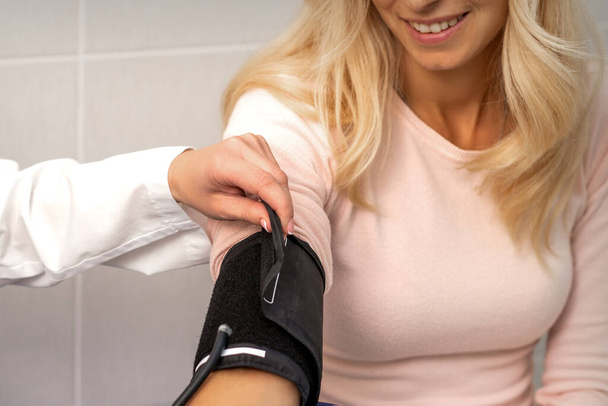 Krankenschwester oder Ärztin legt Tonometer am Arm einer jungen Frau im Krankenhaus an - Foto, Bild