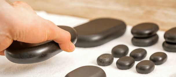 Hand of masseur lays out massage stones on the table in spa salon - Photo, Image