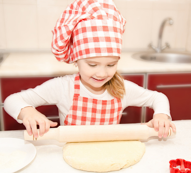 Smiling little girl with chef hat rolling dough - Foto, afbeelding