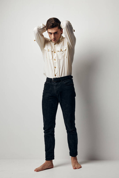 Un chico guapo con una camisa blanca y pantalones sostiene sus manos detrás de su cabeza  - Foto, imagen