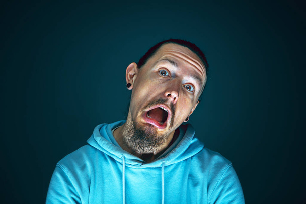 Close up portrait of young crazy scared and shocked man isolated on dark background - Фото, изображение