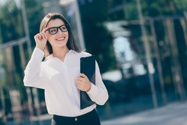 Photo of shiny smiling young lady dressed white formal shirt looking side arm glasses holding clipboard outside - Foto, Imagen