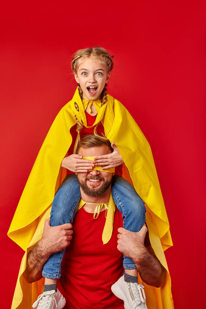 surprised girl sits on neck of father closing his eyes, superhero - Photo, image
