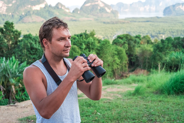 Young man with binoculars in hand watching the wild nature in the tropics. - Zdjęcie, obraz