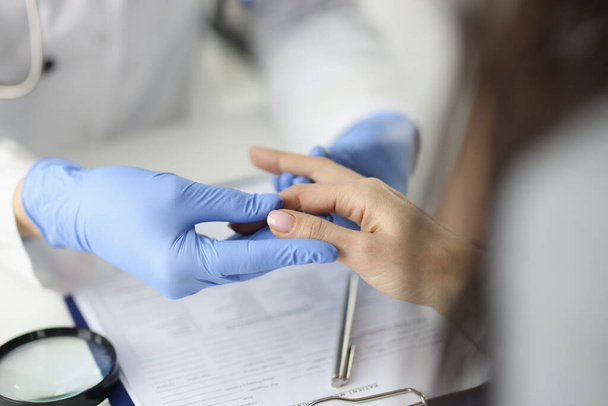 Arzt mit Handschuhen untersucht Finger in Arztpraxis - Foto, Bild