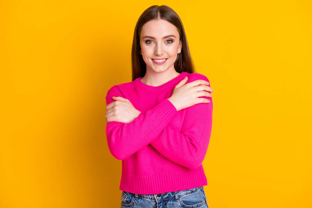Photo of charming young lady cuddle herself look camera toothy smile wear pink pullover isolated yellow color background - Zdjęcie, obraz