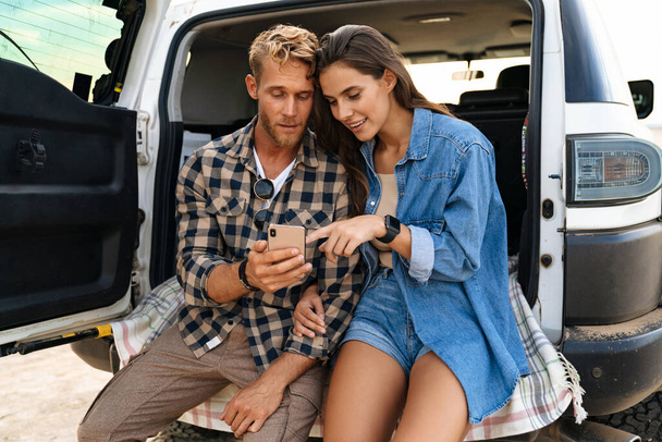 Beautiful couple sitting at the back of car and using smart phones - Φωτογραφία, εικόνα