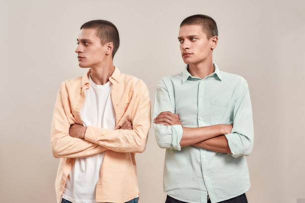 Two young caucasian men, twin brothers looking aside while posing together isolated over beige background - Foto, Imagen