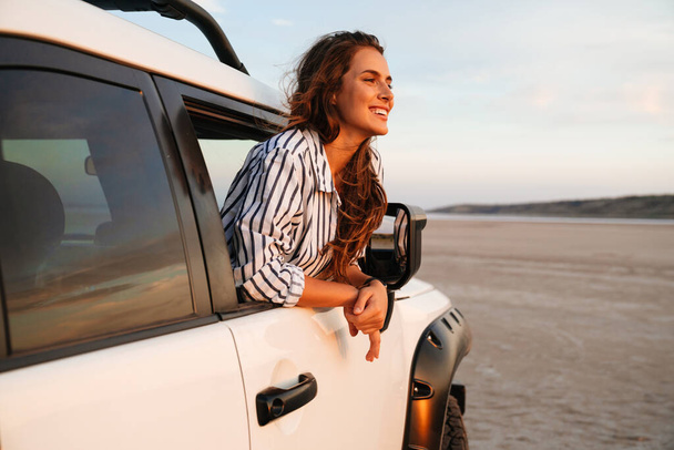 Happy attractive young woman looking out from the car window at the beach - Foto, Imagen