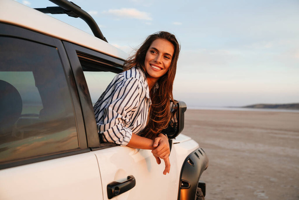 Happy attractive young woman looking out from the car window at the beach - Foto, Bild
