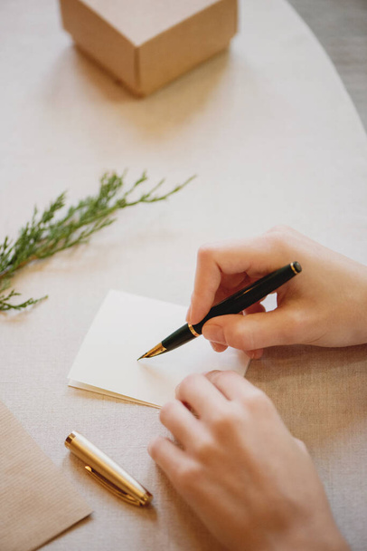 Female hands writing Christmas card on wooden table. - Фото, изображение