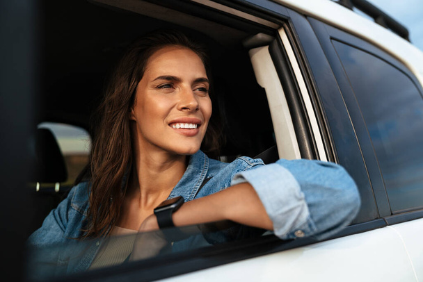 Happy attractive young woman looking out from the car window at the beach - Foto, Imagen