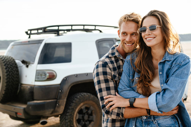Beautiful young smiling couple while bonding to each other and leaning at their car - Foto, Imagen