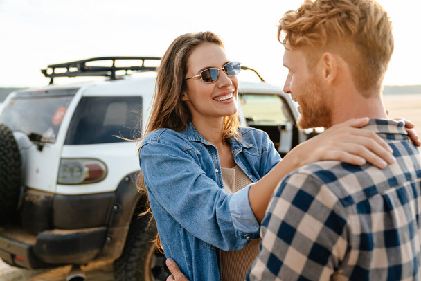 Beautiful young smiling couple while bonding to each other and leaning at their car - Фото, зображення