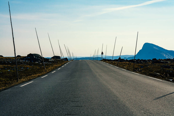 Длинная дорога в горах со стороны дороги с маркировкой палки готовы к зиме, на стороне гора Bitihorn. Размытое прошлое. - Да. Высокое качество фото - Фото, изображение