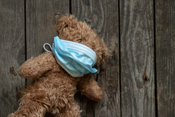 oso marrón de peluche en una máscara médica sobre un fondo de madera, juguete para niños - Foto, Imagen