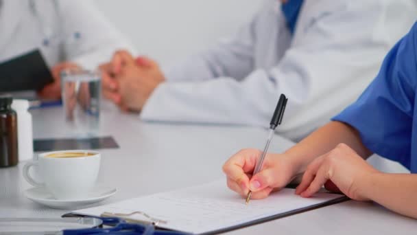 Lähikuva sairaanhoitaja kirjallisesti leikepöydälle aikana lääketieteellinen kokous - Materiaali, video