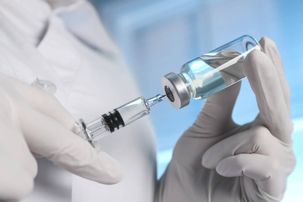 Doctor filling syringe with vaccine from vial on blurred background, closeup - Foto, imagen