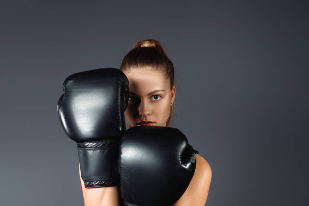 Young businesswoman wearing boxing gloves partially covering her face. Business success concept. High quality photo - Фото, изображение