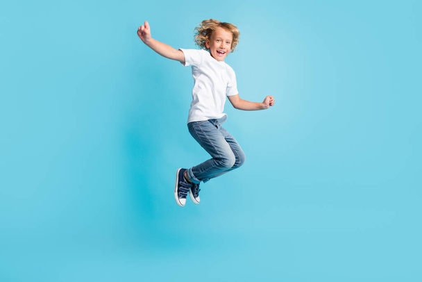 Small kid jump raise hands excited smile wear white shirt jeans sneakers isolated blue color background - Valokuva, kuva