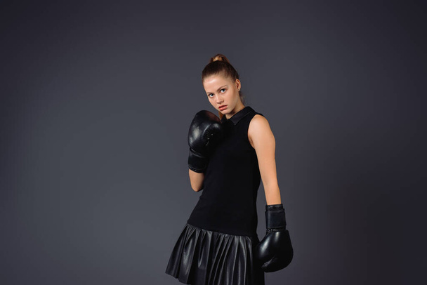 Successful young woman with boxing gloves on a gray background. Confident business concept. High quality photo - Photo, Image
