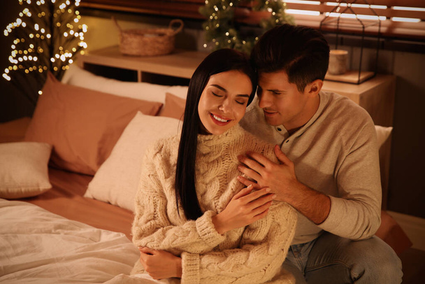 Happy couple sitting on bed in festively decorated room. Christmas celebration - 写真・画像