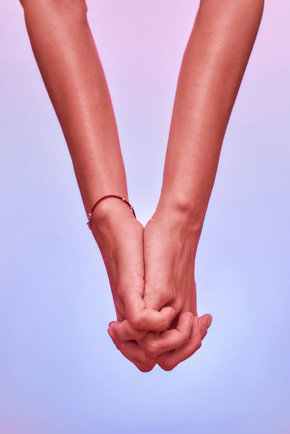 Close up of two girls, sisters holding hands together with fingers crossed isolated over purple background. Support, togetherness concept - Fotoğraf, Görsel