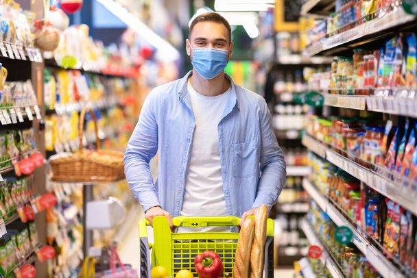 Mladý muž v masce s vozíkem nakupování v supermarketu - Fotografie, Obrázek