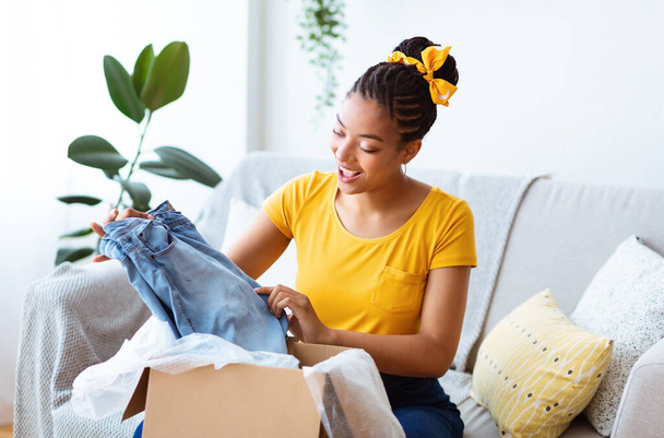 Excited black woman unpacking clothes after online shopping - Фото, зображення