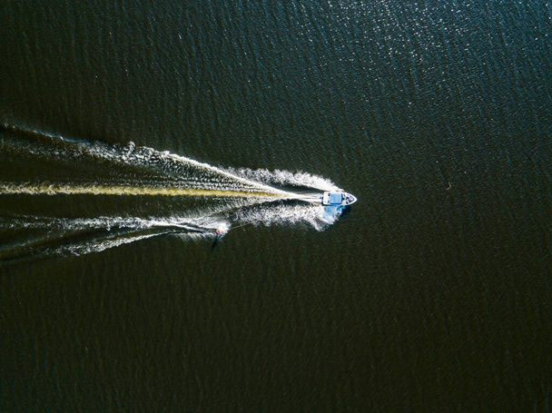 Veduta aerea del drone. Svegliati facendo surf dietro una barca sul fiume in una giornata estiva soleggiata. - Foto, immagini
