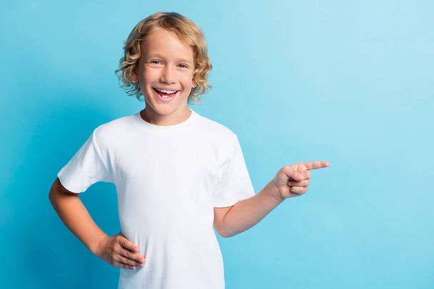 Photo of positive small boy point index finger empty space wear white t-shirt isolated over blue color background - Fotó, kép
