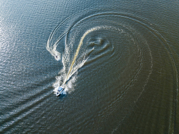 Widok z lotu ptaka. Obudzić surfing za łodzią na rzece w słoneczny letni dzień. - Zdjęcie, obraz