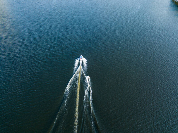 Vue aérienne sur drone. Réveillez-vous en surfant derrière un bateau sur la rivière par une journée d'été ensoleillée. - Photo, image