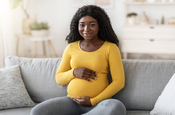 Beautiful black pregnant woman sitting on couch at home - Fotoğraf, Görsel