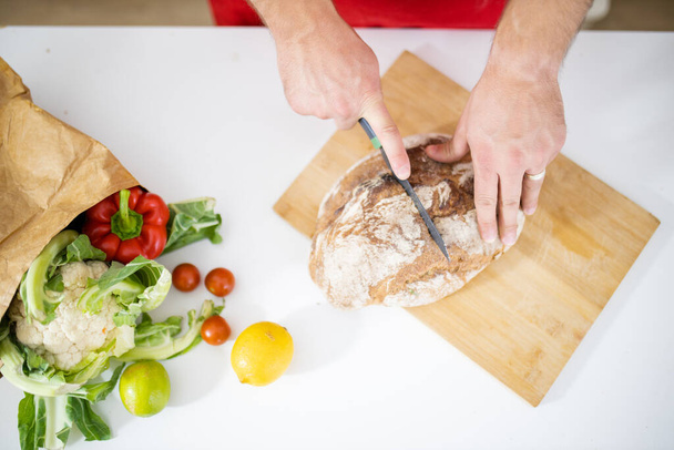 Manos masculinas rebanando pan en una tabla de cortar - Foto, imagen