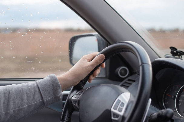 Male hand on the steering wheel of a Mitsubishi car. Autumn rain outside the window. Comfortable SUV driving. - Φωτογραφία, εικόνα