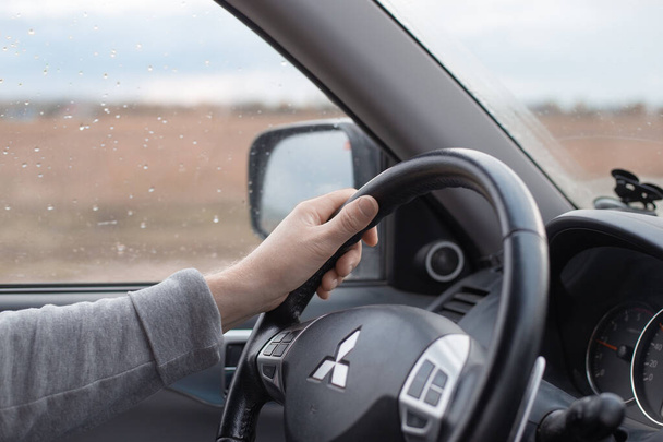 Krasnodar, Russia - 11.02.2020:Male hand on the steering wheel of a Mitsubishi car. Autumn rain outside the window. Comfortable SUV driving - Photo, Image