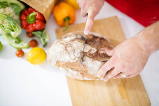 Чоловічі руки нарізають хліб на обробній дошці
 - Фото, зображення