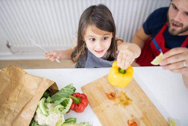 Niña y su padre cortando verduras en una tabla de cortar - Foto, imagen