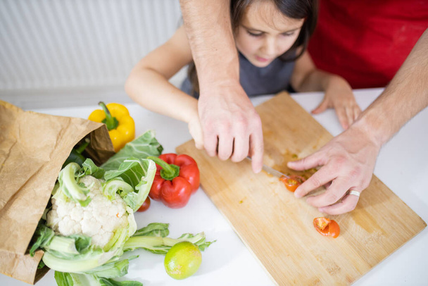Niña y su padre cortando verduras en una tabla de cortar - Foto, imagen