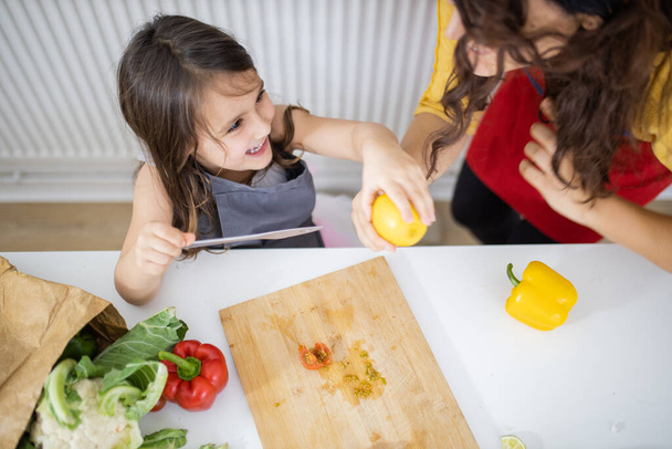 Маленька дівчинка і її мати нарізають овочі на обробній дошці
 - Фото, зображення