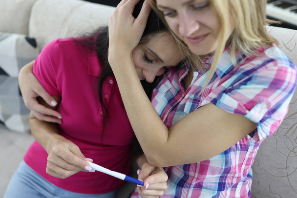 Frau hält Schwangerschaftstest in der Hand, Freundin umarmt. - Foto, Bild