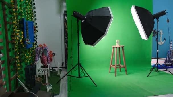 Foto- oder Videostudio mit zwei sechseckigen Studioleuchten. Sanduhr auf grünem Vorhang und festem Stuhl - Filmmaterial, Video
