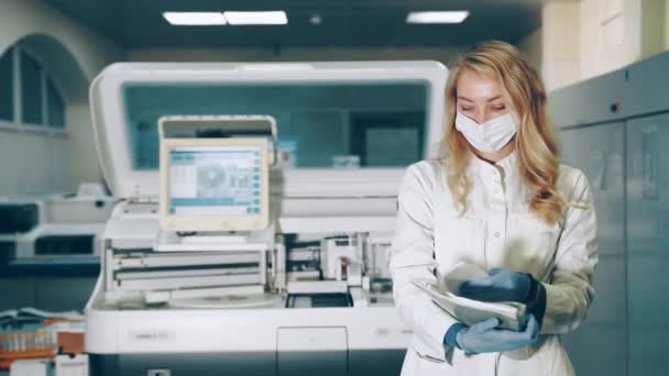 Retrato de um trabalhador de laboratório. Médico feminino em máscara médica protetora em laboratório navega registros em pasta com documentos. - Filmagem, Vídeo