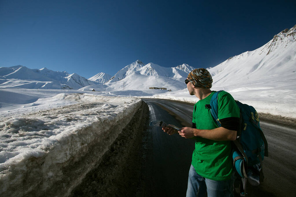 Férfi sportos ruhák és napszemüveg hátizsák túrázás havas hegyekben Georgia. Az ember figyeli a térképet. - Fotó, kép