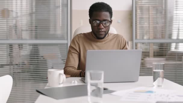 Tracciamento diritto di bell'uomo d'affari afro-americano seduto sul desktop di fronte al computer portatile e comunicare con il partner commerciale via Internet - Filmati, video