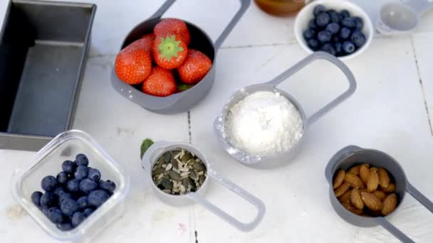 Marjat, jauhot, kaura ja pähkinät valkoisen tiskin yläpuolella olevissa astioissa - Materiaali, video