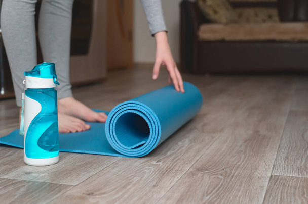 Teenage girl doing fitness exercise, practicing yoga at home. Healthy lifestyle concept. She spreads the yoga mat. Workout at home. Home interior, daytime. - Photo, Image