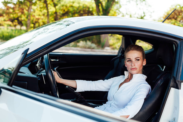 Όμορφη γυναίκα ξανθιά οδηγός πίσω από το τιμόνι ενός λευκού αυτοκινήτου - Φωτογραφία, εικόνα