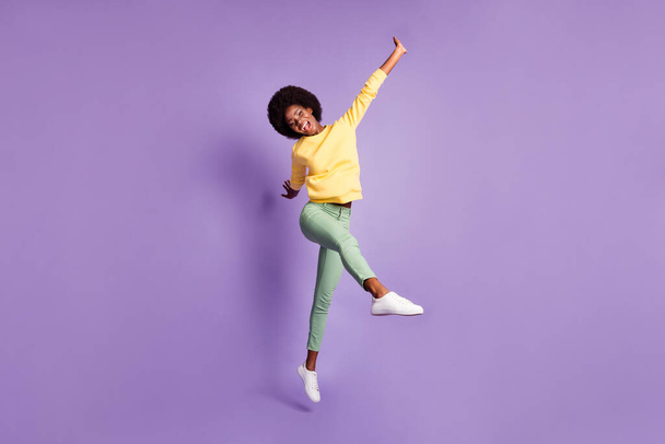Full body photo of excited dark skin girl jump scream wear yellow green pullover isolated over purple color background - Photo, Image